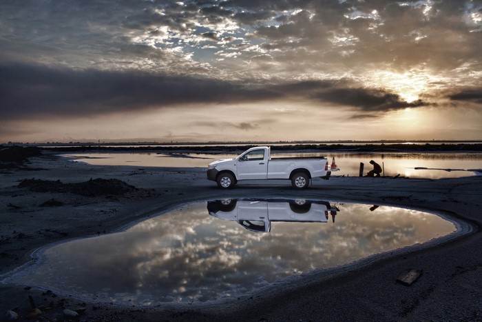 White Toyota Hilux parked by a salt flat at sunset