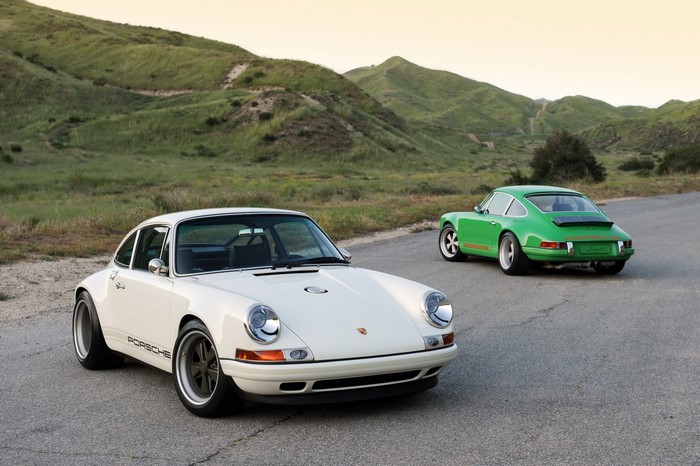 Two Porsche 911s, one white and one green, on a road