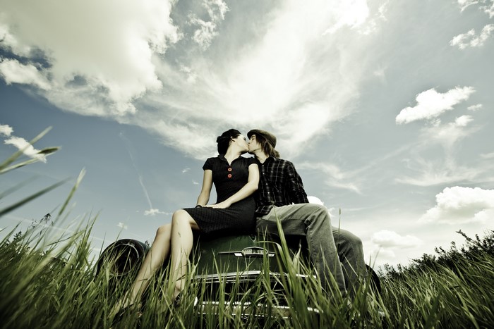 Couple kissing on a vintage car in a field