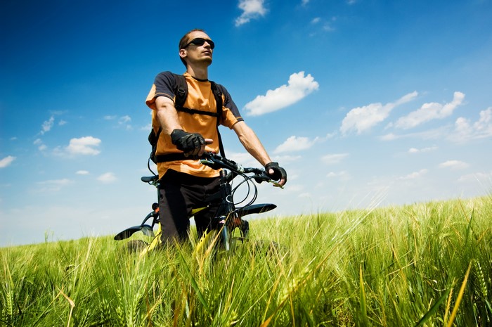 Man with Bicycle in a Field Under Blue Sky