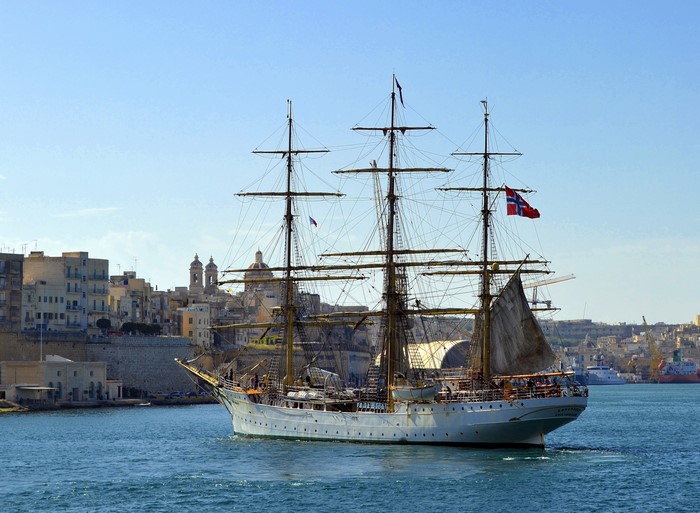 Tall ship sailing in a harbor with city in background
