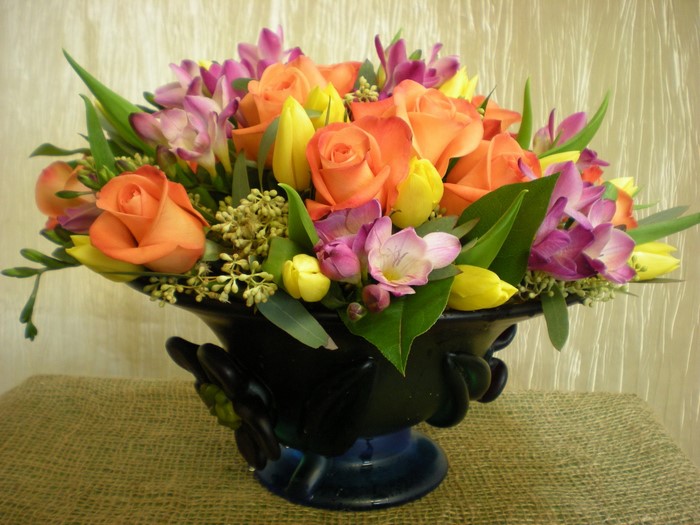 Orange roses and yellow tulips in a dark vase