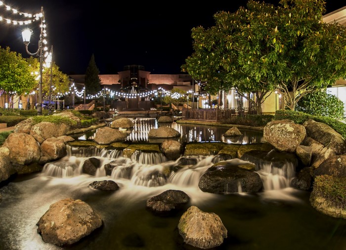 Night scene with illuminated string lights and a rock waterfall pond