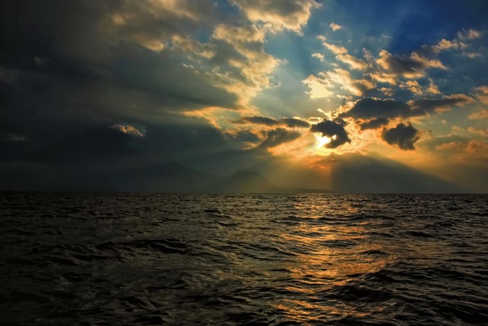 Sunset over a dark ocean with sun rays through clouds