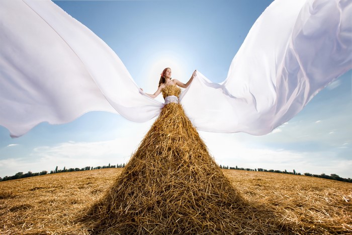 Woman in a straw dress with white fabric in a field