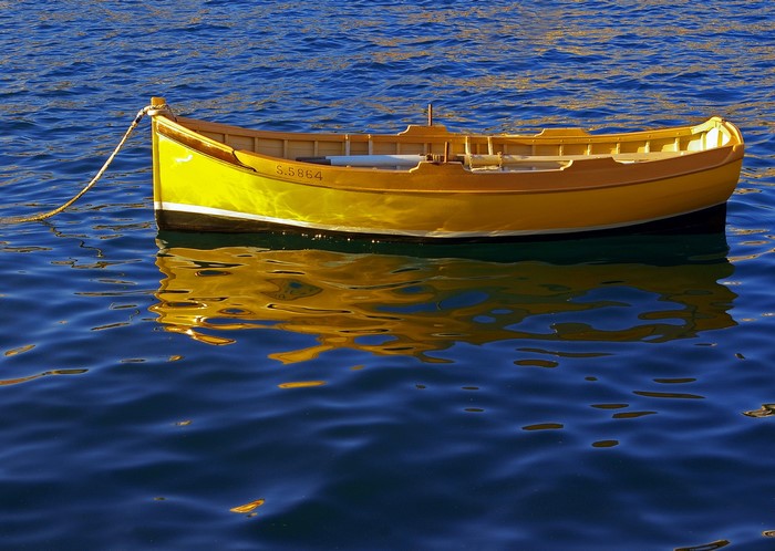 Yellow rowboat on blue water with reflection
