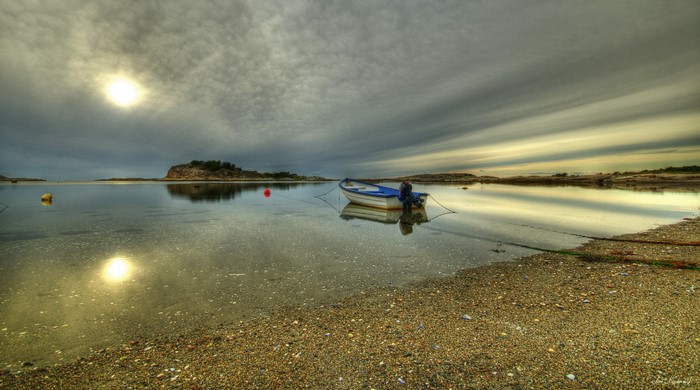 Boat moored in a calm bay with island and sun reflection