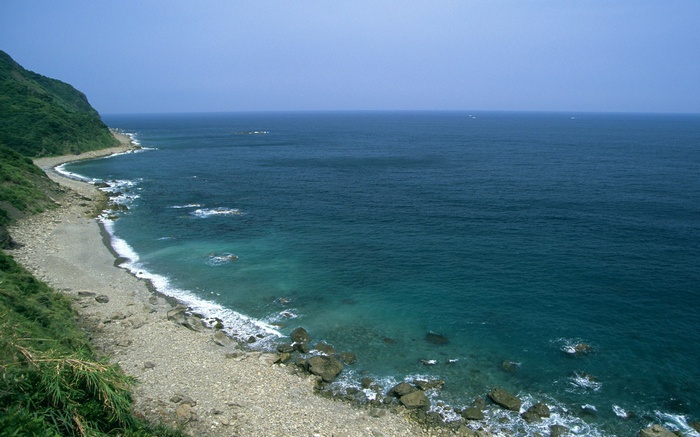 Rocky coastline with blue ocean and green hills