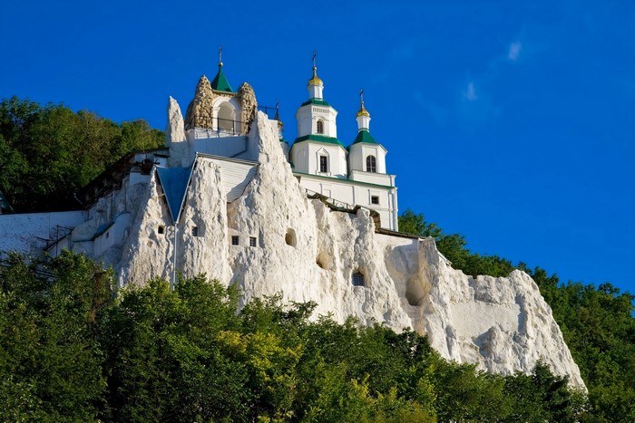 White cave monastery with green domes under blue sky
