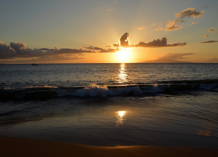 Sunset over the ocean with a sailboat in Maui, Hawaii