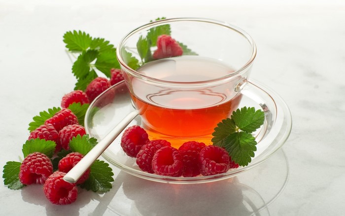 Raspberry tea in a glass cup with fresh raspberries and mint leaves