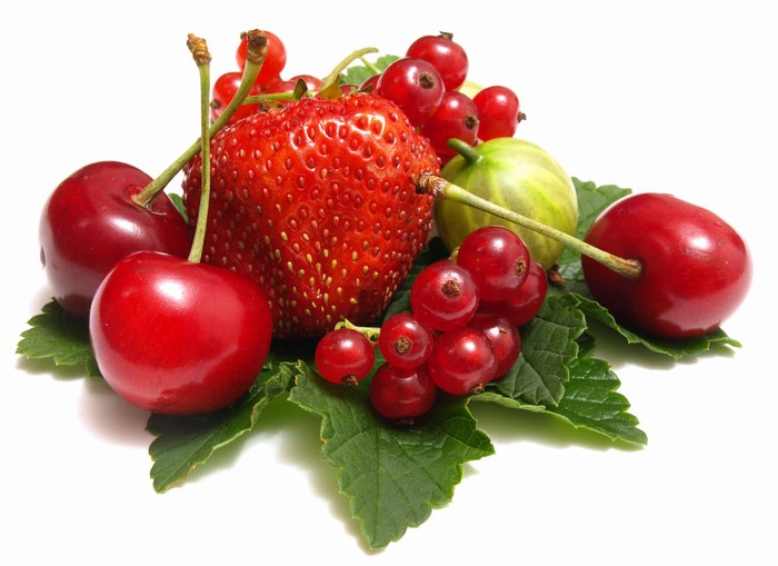 Assortment of fresh berries and cherries on green leaves