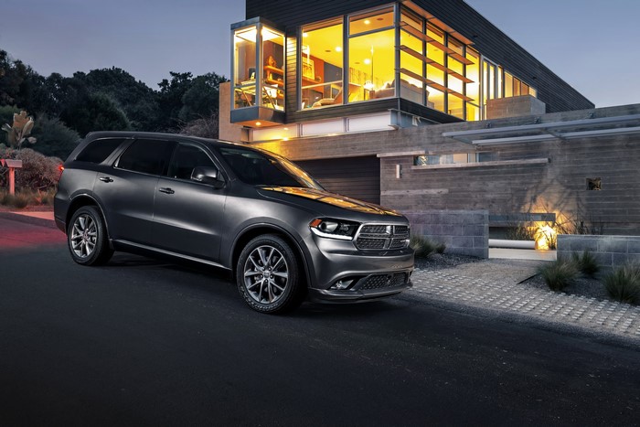 Grey Dodge Durango parked in front of a modern mansion at dusk