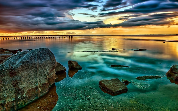 Rocky shore with calm water and dramatic sunset sky
