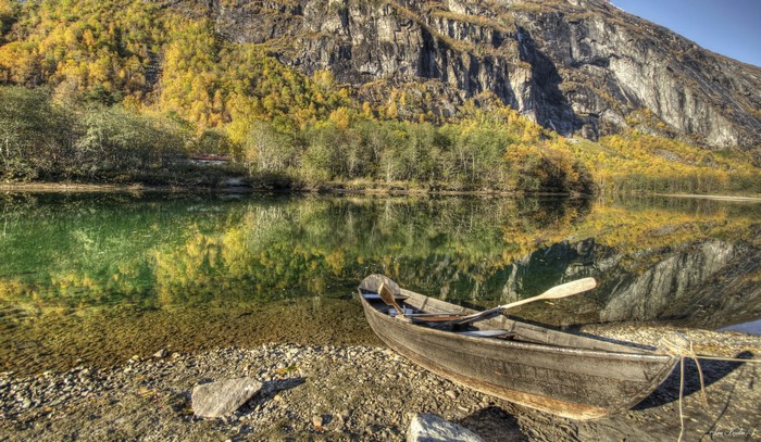 Wooden boat on a rocky shore with autumn trees and mountain reflection
