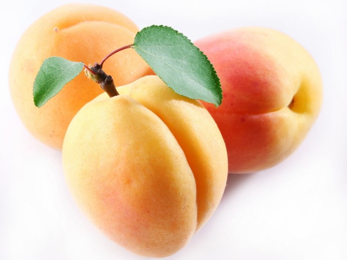 Three ripe apricots with leaves on a white background