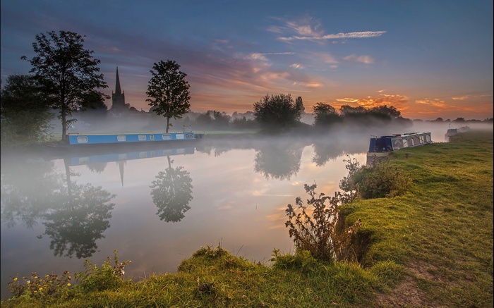 Canal boats on a misty river at sunrise with church spire