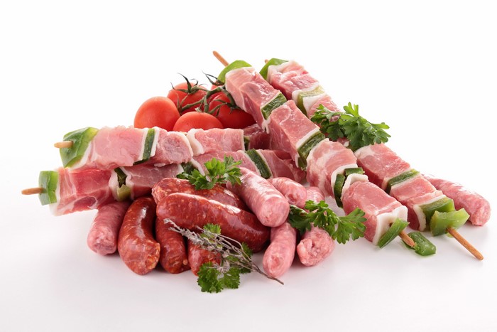 Raw meat skewers, sausages, and tomatoes