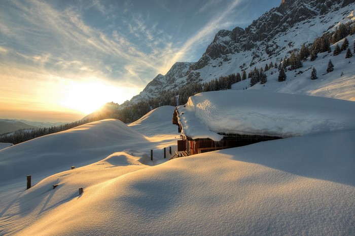 Winter cabin in snowy Austrian mountains at sunset