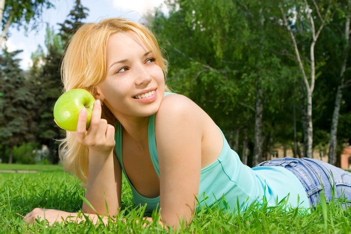 Woman with apple lying on grass