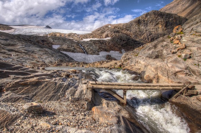 Wooden bridge over a river in a rocky mountain landscape with a glacier