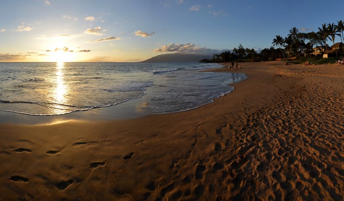 Sunset over a Hawaiian beach with palm trees and ocean waves