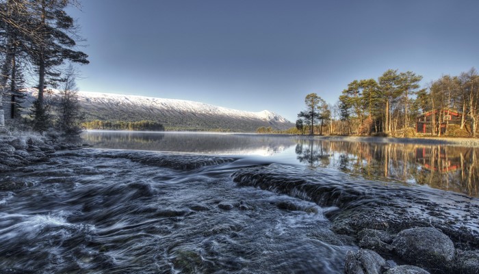 Winter lake with snow-capped mountains and a red cabin