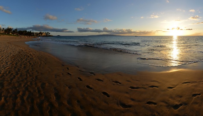 Sunset over a Hawaiian beach with footprints in the sand