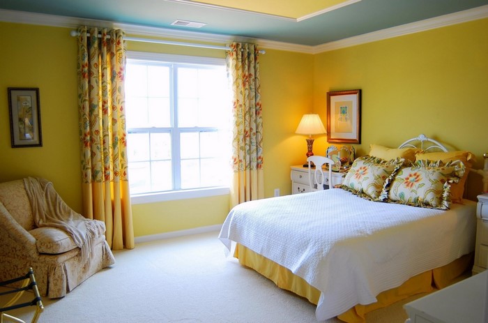 Yellow bedroom with floral curtains and a white bed