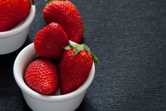 Strawberries in white bowls on a dark surface
