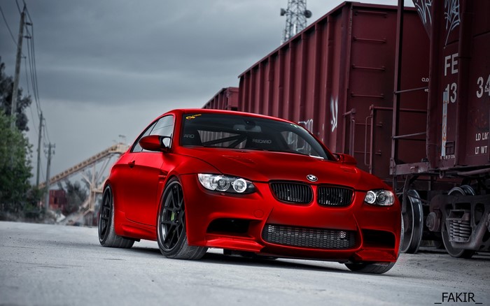 Red BMW M3 Coupe parked next to train cars