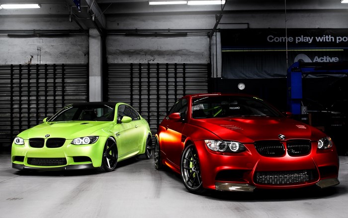 Two BMW M3s, one red and one lime green, in a garage