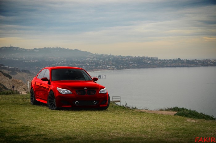 Red BMW M5 on a grassy cliff overlooking the ocean