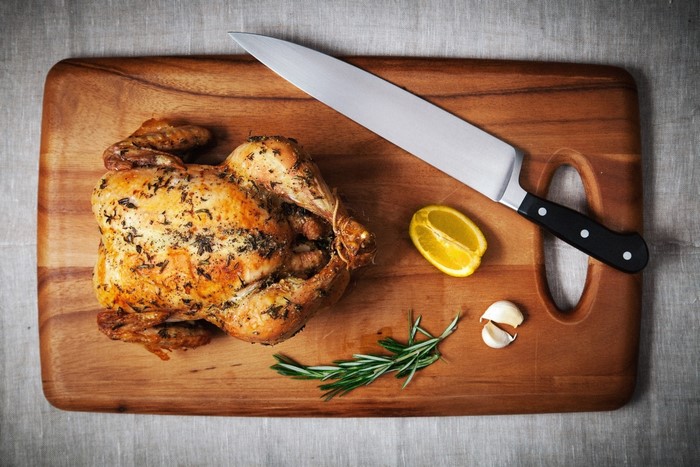 Roast chicken with knife, lemon, garlic, and rosemary on cutting board