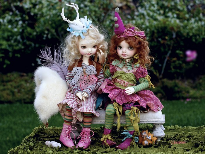 Two dolls dressed in whimsical outfits sitting on a bench