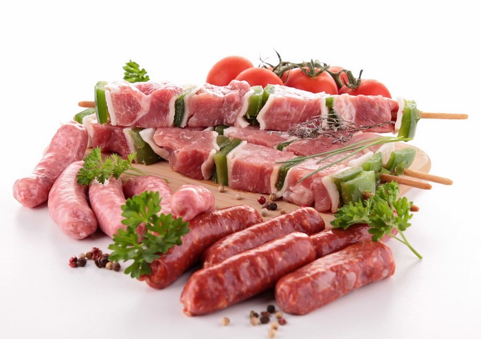 Raw meat skewers, sausages, tomatoes, and herbs on a board