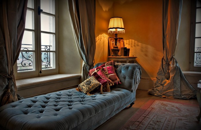 Elegant chaise lounge with pillows near a window and lamp