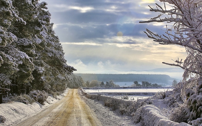Snowy road through a winter forest with distant hills