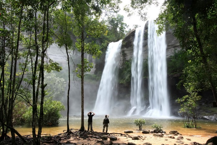 Two people admire a large waterfall in a lush forest