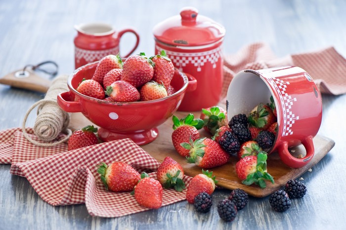 Strawberries and blackberries in red bowls and a mug