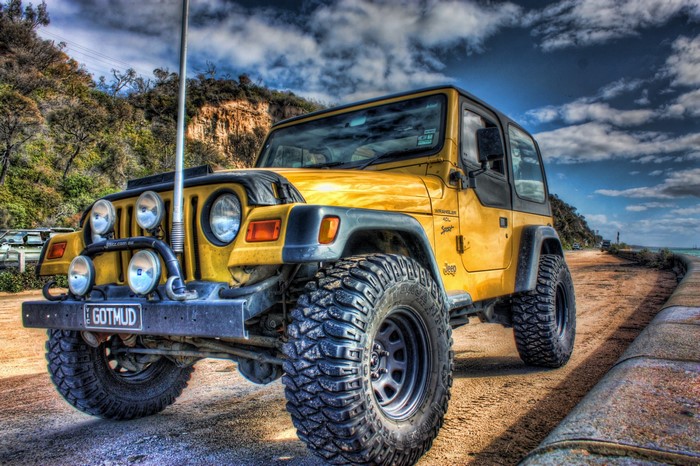 Yellow Jeep Wrangler with large tires on a dirt road
