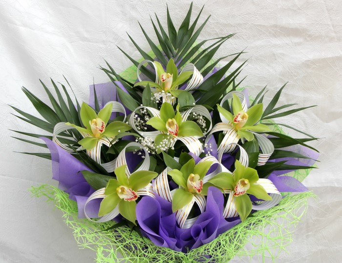 Green orchids in a bouquet with palm leaves and ribbons