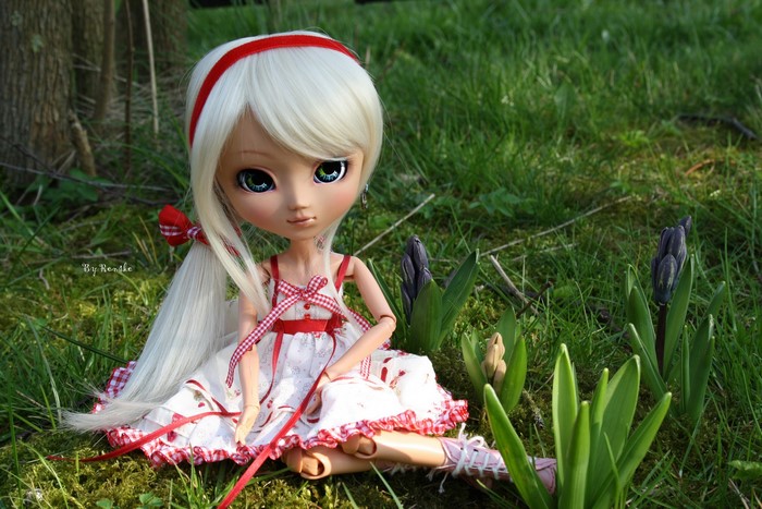Doll with blonde hair and red headband sitting in grass