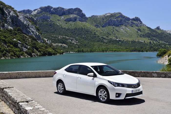 White Toyota Corolla parked by a lake with mountains