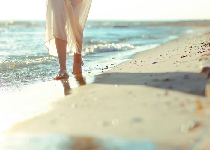 Legs walking on a sandy beach by the sea