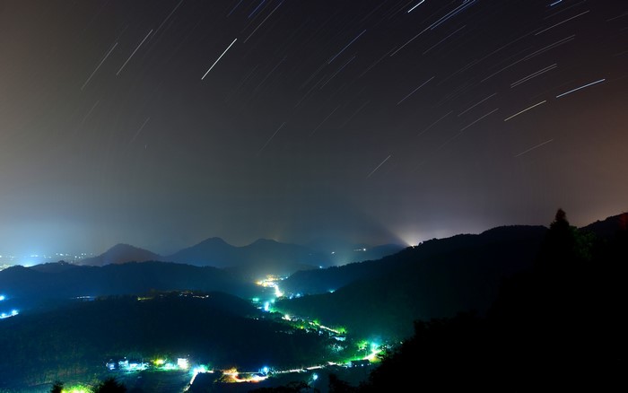 Star trails over mountains and a valley at night