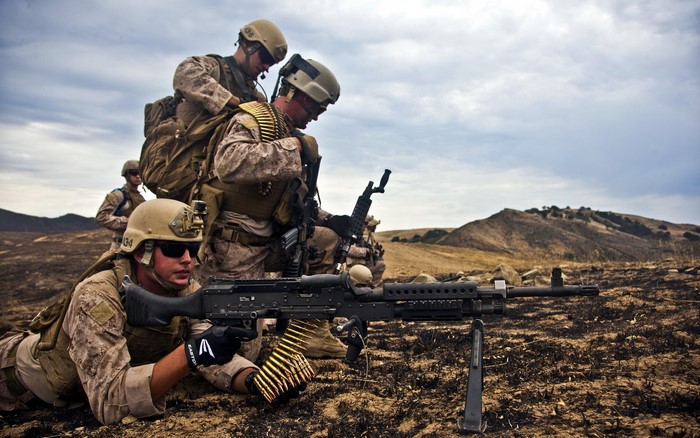 Soldiers with machine guns in a dry, hilly landscape