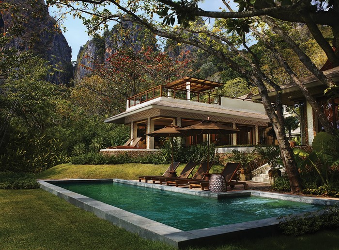 Resort pool with loungers and umbrellas near limestone cliffs in Thailand