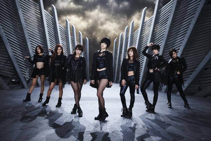 Six women in black outfits posing in front of a futuristic structure