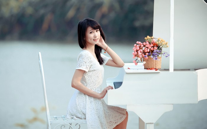 Asian woman in white dress by a piano with flowers